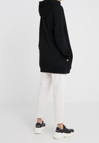 Sudadera negra con capucha y bolsillos amplios, ajuste relajado y puños acanalados. Combinada con pantalones blancos ajustados y zapatillas negras gruesas.