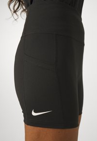 Črne atletske kratke hlače iz raztegljivega materiala, z visokim pasom in majhnim belim logotipom Nike na spodnji levi strani.