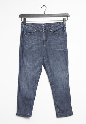 Jeansy z ciemnego niebieskiego denimu z delikatnym wyblaknięciem, design pięciu kieszeni, zapięcie na guzik i zamek, wiszące na czarnym wieszaku na białym tle.