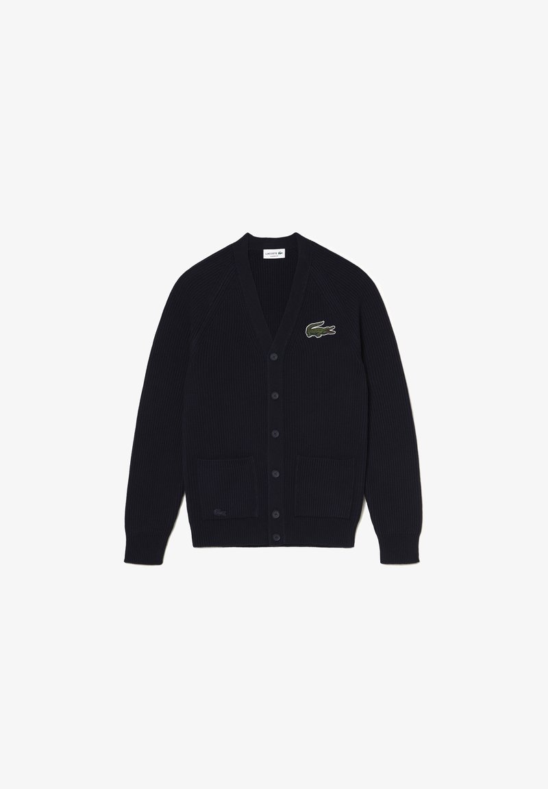 Cardigan noir en maille côtelée avec col en V, fermeture par boutons, deux poches avant et un logo crocodile vert sur la poitrine gauche.
