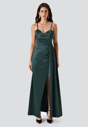 Langes, smaragdgrünes Satin-Kleid mit tailliertem Oberteil, schmalen Trägern und einem hohen Schlitz bis zum Oberschenkel. Es hat Raffungselemente und einen fließenden Rock.