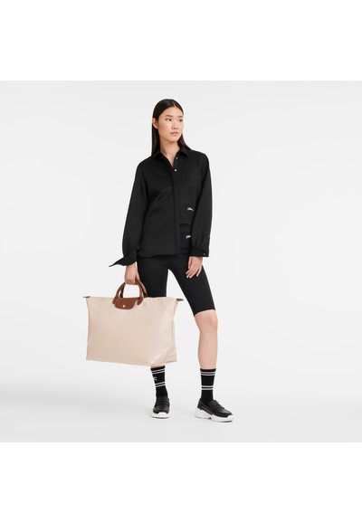 Black long-sleeve shirt, buttoned, with a relaxed fit. Black bike shorts. Light beige tote bag with brown handles. Black shoes and striped socks.