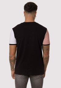 Camisa de manga corta en bloque de color negro y rosa con dobladillo redondeado y costuras en contraste. Tejido de algodón con una textura suave.