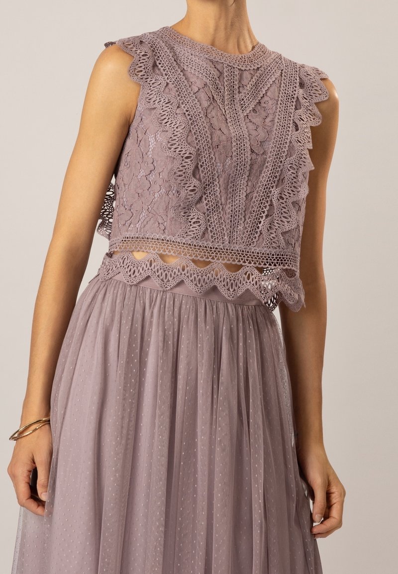 Top crop en dentelle de lavande douce avec des bords à volants, des motifs complexes et un design ouvert, associé à une jupe en tulle fluide et transparente.