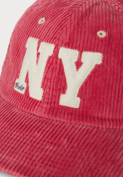 Gorra de pana roja con grandes letras blancas bordadas "NY" en el frente y detalles sutiles de costura. Tela texturizada con forma redondeada.