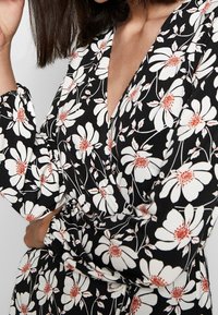 Blommig klänning med svart bakgrund, med stora vita blommor och orangea mittenpartier. Långa ärmar med samlade manschetter. V-ringad design.