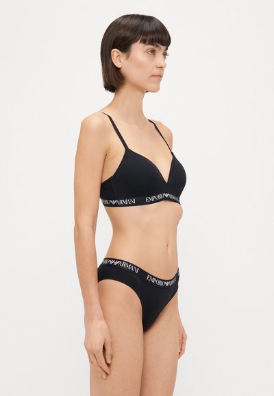 Melnas apakšveļas komplekts, kas sastāv no braletes ar V veida izgriezumu un plānām siksniņām, kopā ar atbilstošām bikini apakšbiksēm. Ar logotipa joslas detaļām.