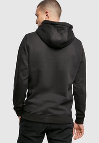 Felpa nera con cappuccio, dal tocco morbido, con polsini elasticizzati e tasca a marsupio. Caratterizzata da un design semplice e minimalista.