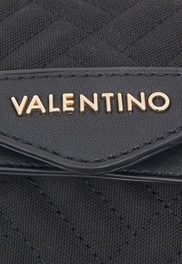 Svart kviltat tygplånbok med guld "VALENTINO"-logotyp. Har släta läderdetaljer och en texturerad yta. Kompakt kvadratisk form.