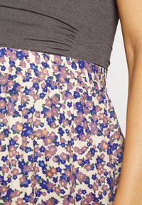 Saia floral com base creme e flores roxas e azuis, cintura elástica e design pregueado. Acompanhada por um top cinza escuro.
