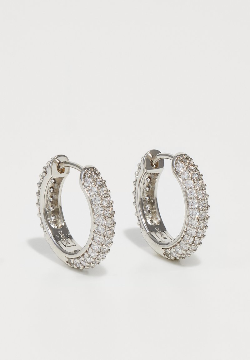 Strieborné kruhové náušnice ozdobené čírymi kamienkami, s hladkým povrchom a zaobleným tvarom. Geometrický dizajn s trblietavými detailmi.