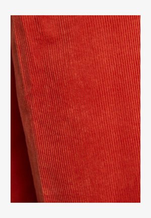 Czerwona tkanina sztruksowa z pionowymi prążkami, cechująca się miękką fakturą. Równomierny kolor i wyraźne linie tworzą jednolity wygląd.