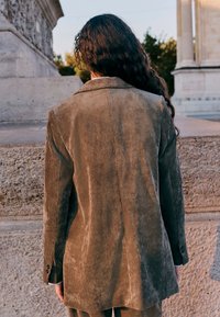 Brown corduroy blazer with a tailored cut, visible vertical ribbing texture, notched lapels, and buttoned cuffs.