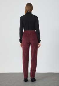 Bordeaux corduroy broek met een hoge taille, zijzakken en twee achterzakken. Gecombineerd met een fitted zwart shirt met lange mouwen.