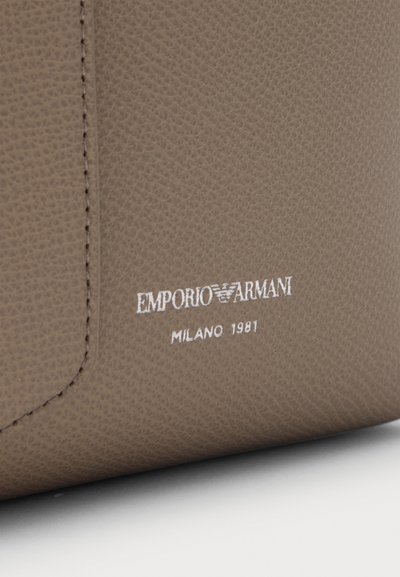Gros plan d'une surface en cuir texturé taupe avec le logo blanc Emporio Armani Milano 1981 imprimé près de la couture cousue.