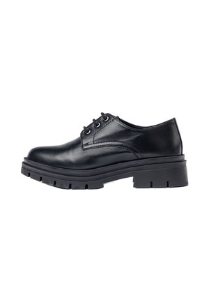 Zapato oxford de cuero negro con punta redondeada, acentos cosidos y una suela de goma negra gruesa y resistente con un patrón de profundidad.