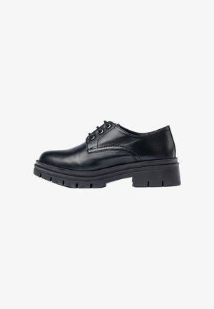 Zapato oxford de cuero negro con punta redondeada, acentos cosidos y una suela de goma negra gruesa y resistente con un patrón de profundidad.
