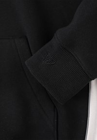 Sort hættetrøje med ribbede manchetter; har en tekstureret overflade og en lille broderet logo på manchetten; sidepanel i kontrastfarve.