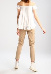 Bílý top bez ramínek s volánkovým lemem, spárovaný s béžovými cargo kalhotami a bílými kotníkovými botami. Jednoduchý, uvolněný střih.