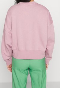 Ljusrosa, kort sweatshirt med en avslappnad passform, ribbade ärmslut och halsringning, i kombination med gröna skräddarsydda byxor. Mjuk tygstruktur.