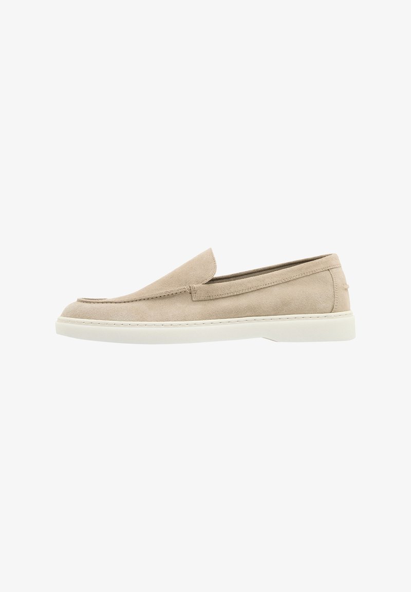 Mocassin beige en daim sans lacets avec semelle en caoutchouc blanche et détails cousus, présenté de profil sur fond blanc.