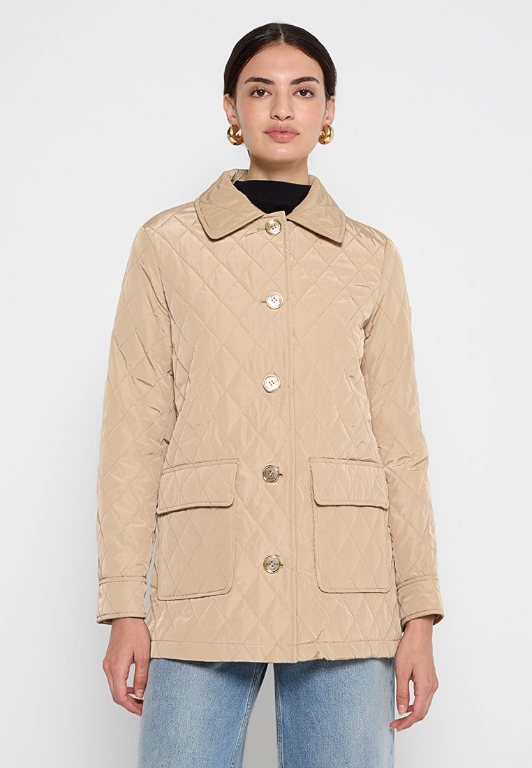 Giacca trapuntata beige con colletto, bottoni frontali e due tasche a pattina. Texture liscia con motivo a diamante e dettagli in metallo dorato sui bottoni.