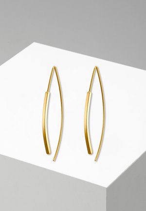 Paar dünne, gebogene Goldohrringe mit minimalistischem, verlängertem Design, dargestellt auf einer weißen und grauen geometrischen Oberfläche.