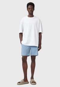 Camiseta de algodón blanca de gran tamaño, pantalones cortos azul claro y sandalias de dedo marrones. Diseño simple sin patrones o acentos visibles.