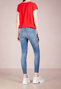 Camisa roja de manga corta combinada con jeans ajustados azules y zapatillas blancas. La camisa tiene un escote redondeado y los jeans cuentan con bolsillos traseros.