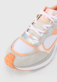 Lightweight sneaker with a mesh upper in white, peach, and silver accents. Features a gray suede toe cap and textured orange outsole.