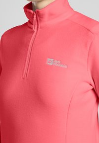 Pullover in pile di colore rosa acceso con colletto alto e zip a metà. Presenta un logo Jack Wolfskin in azzurro chiaro sul petto.