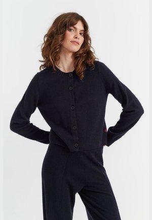 Cardigan corto navy realizzato in morbido tessuto, caratterizzato da un colletto rotondo, maniche lunghe, chiusura frontale con bottoni e polsini e orlo a coste.