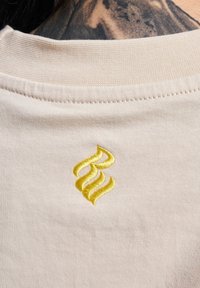 Beige cotton t-shirt featuring a yellow embroidered design on the back neckline. Smooth texture with flat seams.