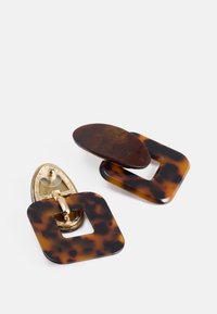 Ohrringe im Schildpatt-Muster mit einer Clip-Verschluss in Goldton. Das Design beinhaltet eine ovale und quadratische Form und hebt eine glänzende Oberfläche hervor.