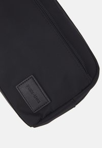 Housse d'ordinateur portable noire en nylon, de forme plate, avec fermeture zippée et un patch en cuir texturé étiqueté "PIER ONE."