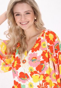 Blusa floreale con un vivace motivo di fiori rossi, rosa e gialli su sfondo bianco. Tessuto leggero, design a scollo a V.