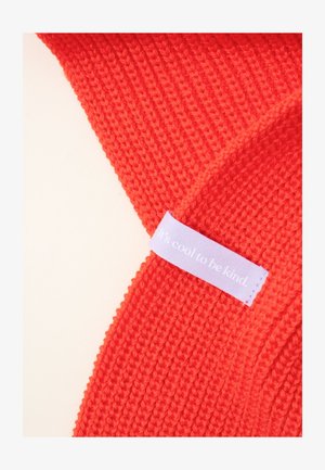 Rotes gestricktes Accessoire mit gerippter Textur. Verfügt über ein helllila Etikett mit dem Text "Es ist cool, freundlich zu sein."