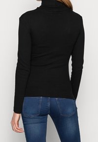 Svart polotröja, ribbat mönster, slim fit, långa ärmar. Tillsammans med blå jeans med bakfickor och lätt blekning.