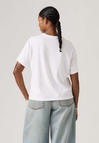 Λευκό βαμβακερό t-shirt με κοντά μανίκια, άνετη εφαρμογή και στρογγυλή λαιμόκοψη, συνδυασμένο με ανοιχτό μπλε τζιν παντελόνι με φαρδιά μπατζάκια.