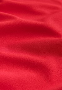 Tissu rouge lisse avec des plis doux et une surface légèrement texturée, éclairé de manière uniforme pour mettre en valeur sa couleur riche et son tomber.