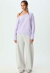 Lavendelfarbenes, übergroßes Strickoberteil mit einem schulterfreien Design, kombiniert mit lockeren grauen Sweatpants und hellgrauen Sneakers. Einfache, weiche Texturen.
