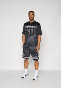 Black sports jersey with white pinstripes, featuring "RAIDERS" and "60" on the front. Paired with matching shorts and white sneakers.