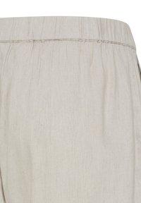 Pantalon beige clair avec ceinture élastique, coutures visibles et texture de tissu doux, présenté en gros plan.