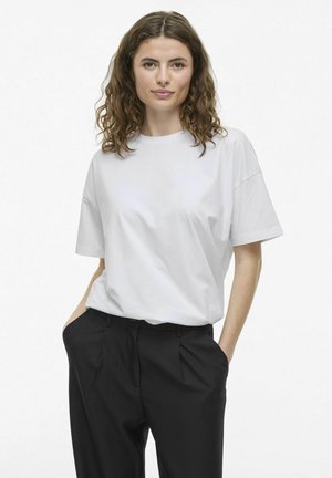 Camiseta de algodón blanca con cuello redondo y mangas cortas, con un corte relajado. Combinada con pantalones negros lisos.