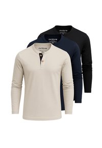 Tres camisetas de manga larga estilo Henley en beige, azul marino y negro, dispuestas en capas de delante hacia atrás con los cuellos abotonados.