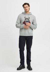 Šedá mikina s kapucňou a grafikou panda v slnečných okuliaroch, s rebrovanými manžetami a lemom, v kombinácii s tmavými nohavicami a čiernymi topánkami.