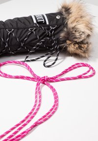 Botte d'hiver noire avec bordure en fourrure et lacets noirs, à côté d'un lacet rayé rose et blanc noué sur une surface blanche.