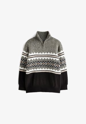 Pull avec col demi-zip en gris, noir et blanc avec des motifs géométriques et en zigzag sur la poitrine et les manches, porté en extérieur.