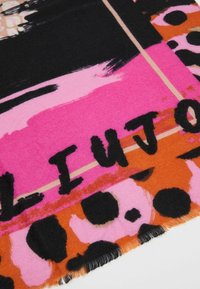 Tissu multicolore présentant des motifs abstraits audacieux en rose et orange avec des accents noirs. Les bords sont frangés, affichant des textures variées.