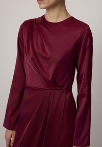 Burgundia satiinkleit, millel on pikad varrukad, ümmargune kaelus, kehakujundus ja voldid vöökohtadel.